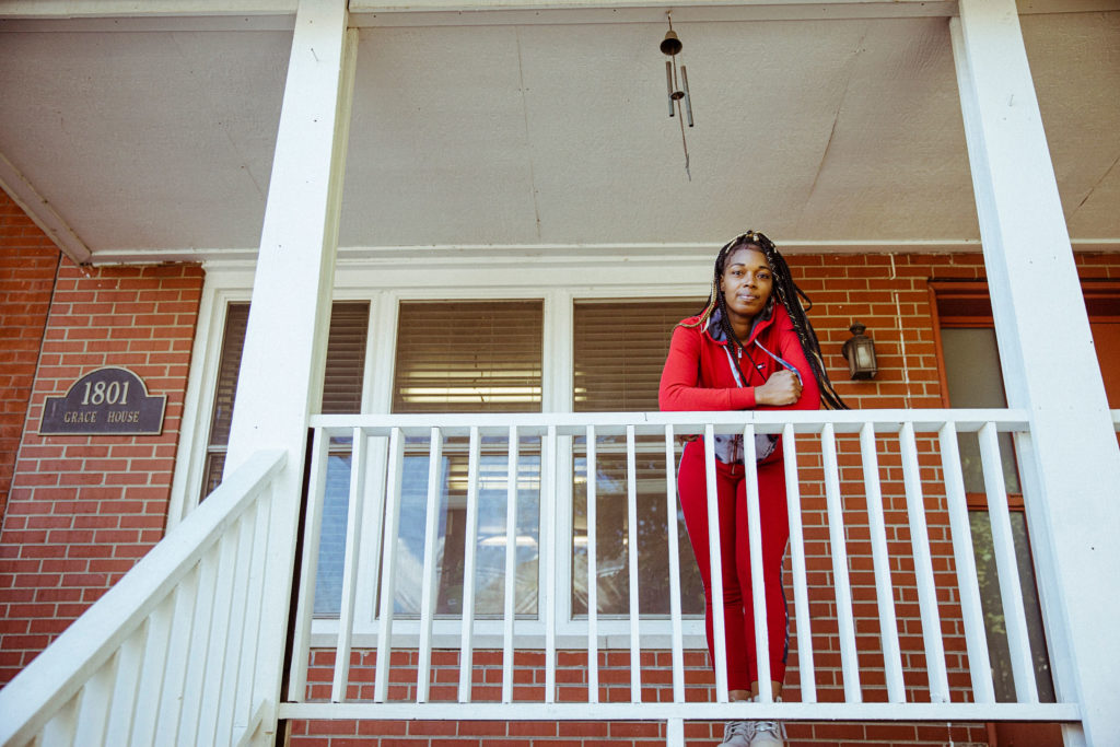 a Black woman leans over a railing on a porch