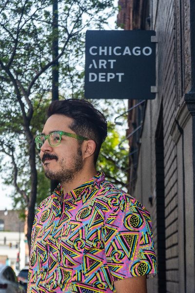 Carlos Flores posing with a slight smile outside in front of Chicago Art Dept sign.