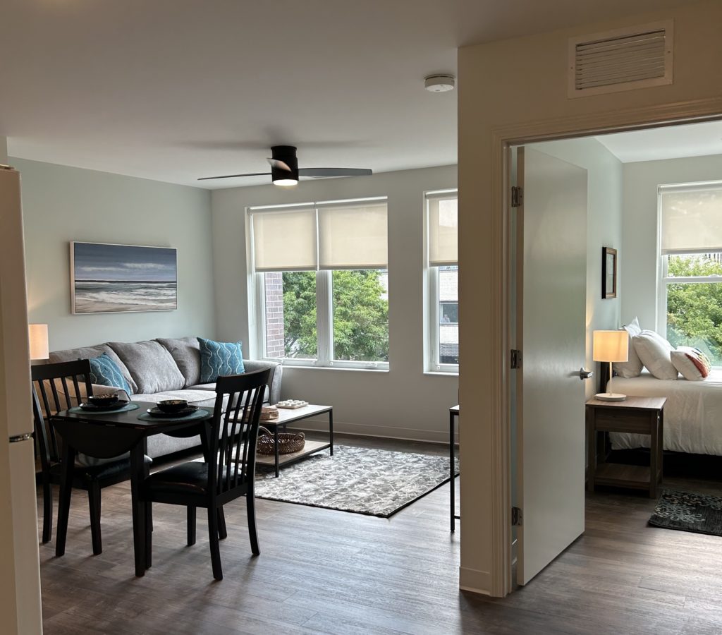 A view of one of the 16 units recently opened during Impact Behavioral Health's ribbon cutting. The picture shows a artfully decorated living room, dining table, and bedroom with a view of greenery outside the window. 