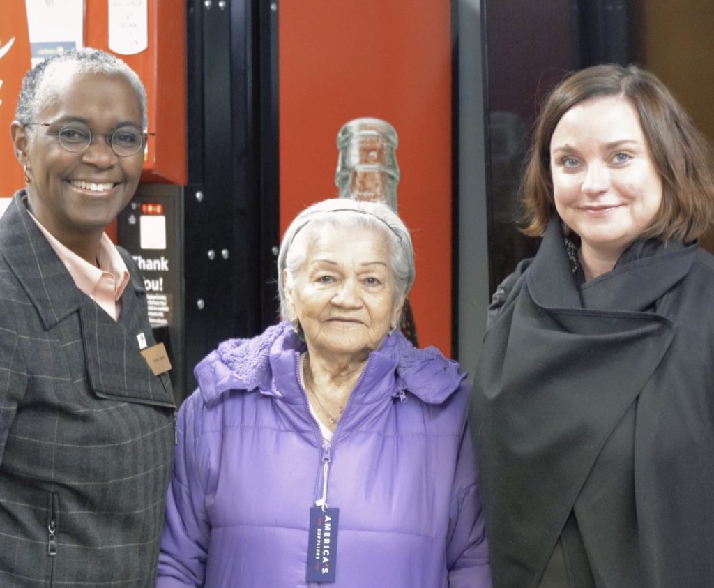 Three smiling women at a CHA Winter Wear distribution event.